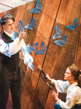 An image from the play in which a puppeteer controls blue butterflies around Charles Darwin