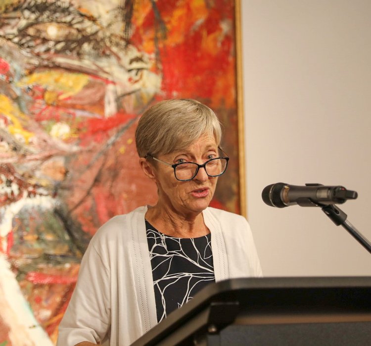 Kathryn Fry speaks at a podium with an abstract painting behind her.
