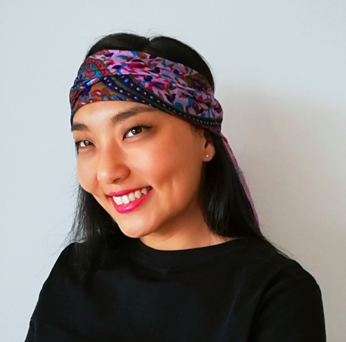Lisa Nan Joo wears a colourful scarf on her head and smiles at the camera.