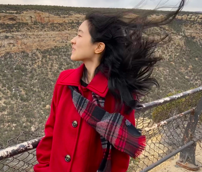 Lucy Zhang stands in nature with wind in their hair.