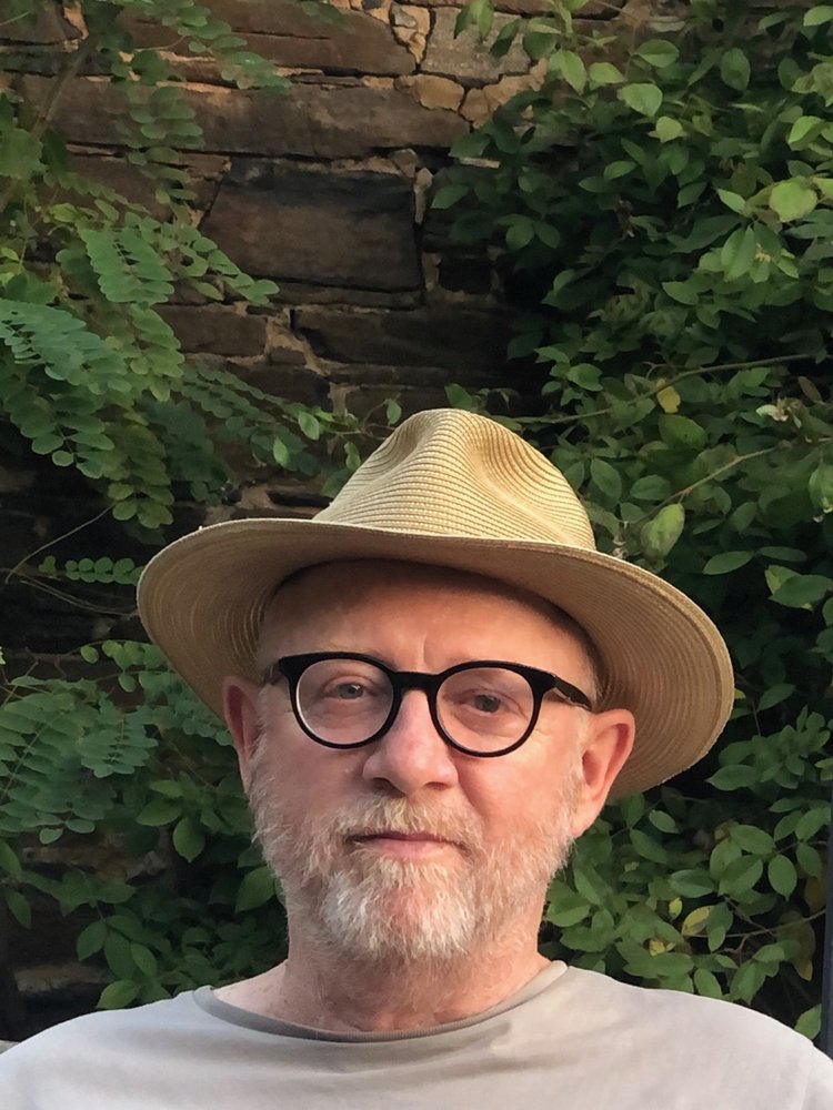 Mark O’Flynn wears classes and a straw hat and looks at the camera.